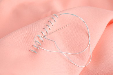 Photo of Sewing needle with thread and stitches on coral cloth, closeup