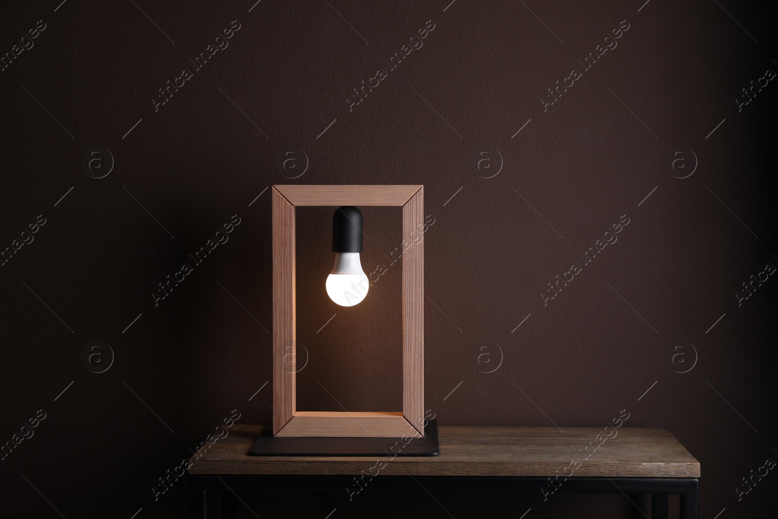 Photo of Wooden table with lamp near brown wall in room, space for text