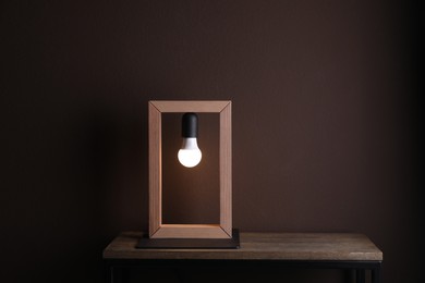 Photo of Wooden table with lamp near brown wall in room, space for text