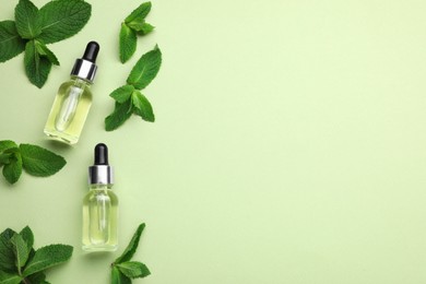 Photo of Bottles of essential oil and mint on light green background, flat lay. Space for text
