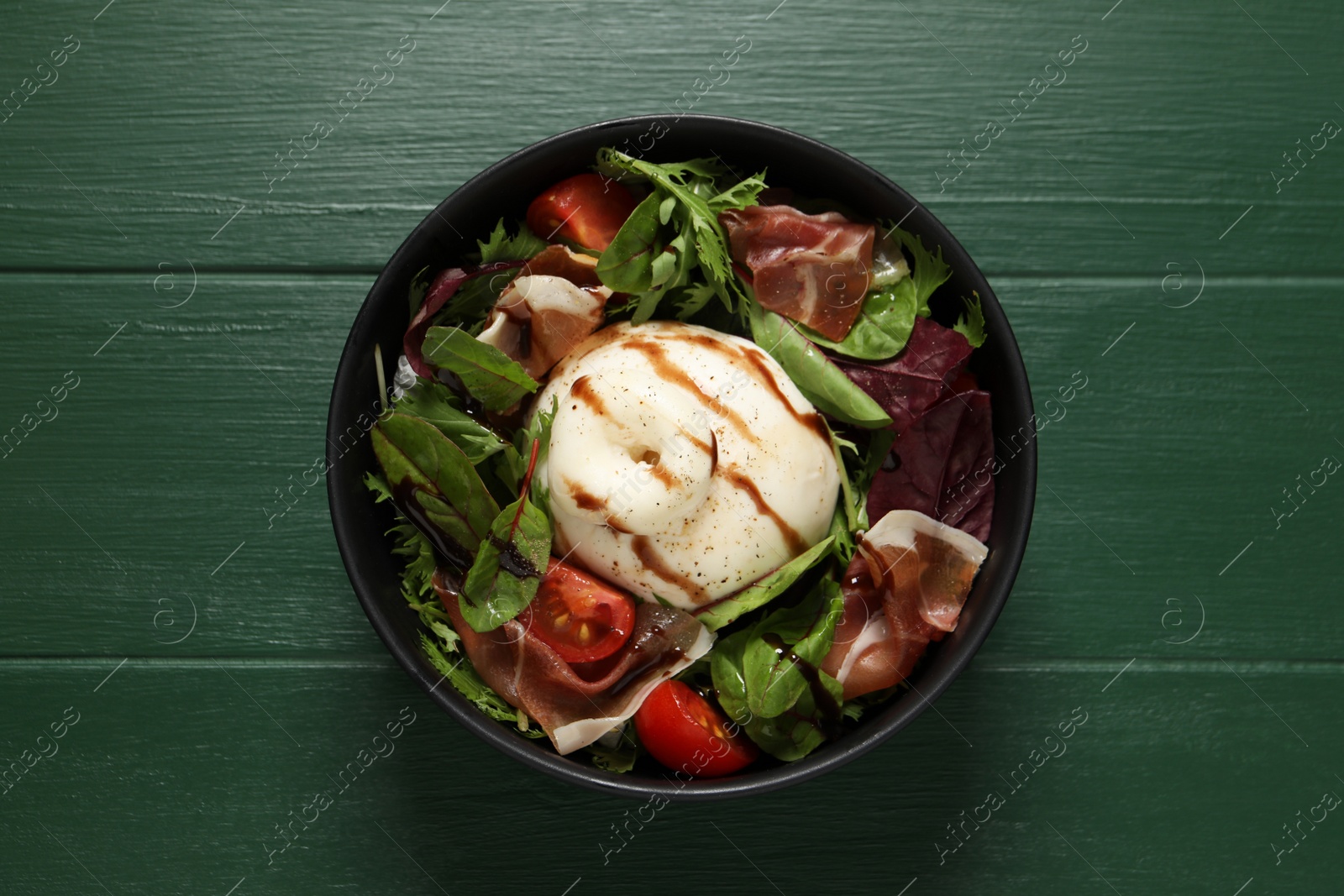 Photo of Delicious burrata salad on green wooden table, top view