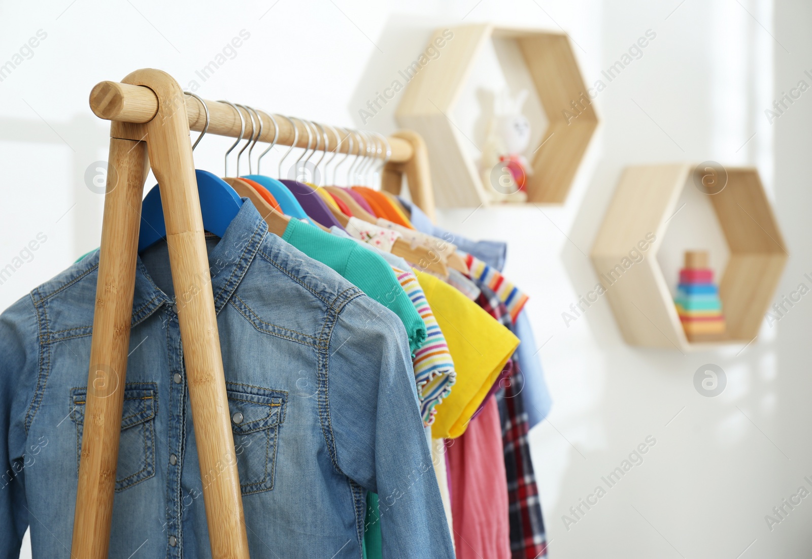 Photo of Different child's clothes hanging on rack indoors, closeup. Space for text