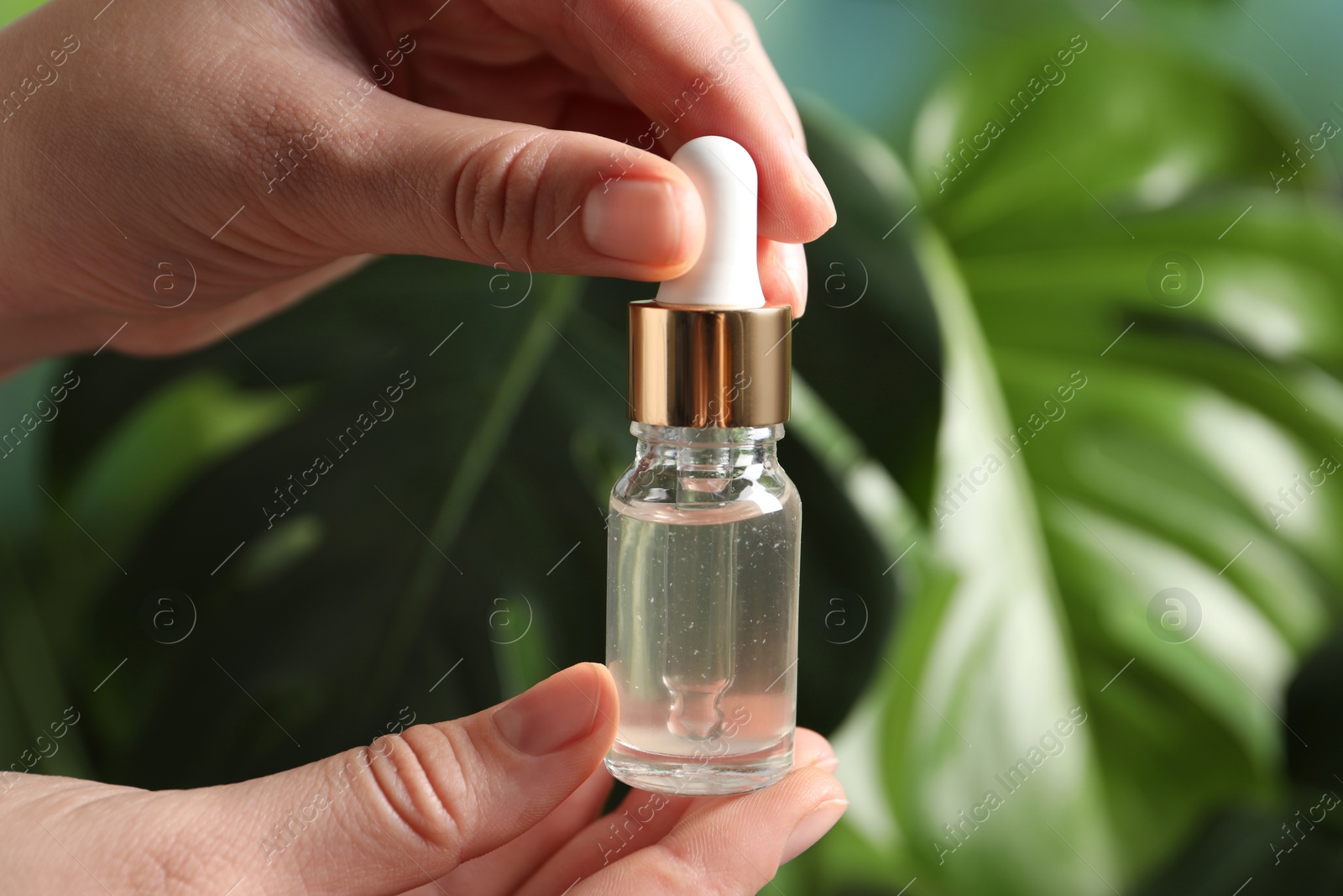 Photo of Woman with bottle of cosmetic serum on blurred background, closeup