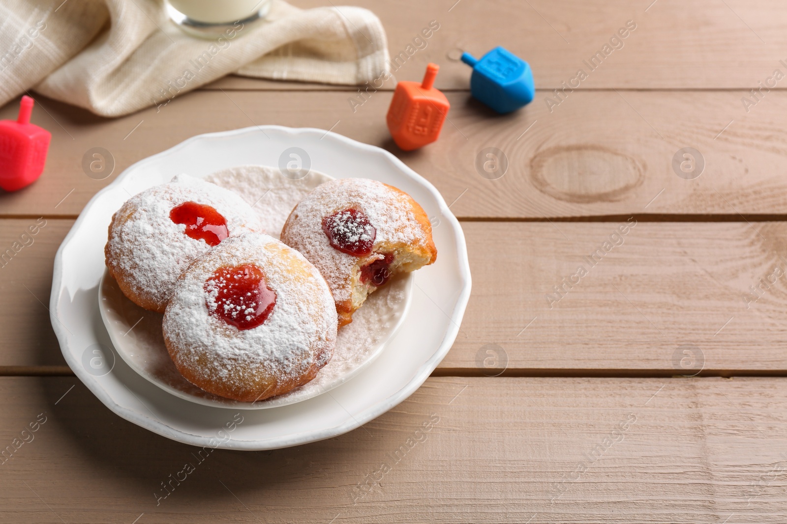 Photo of Hanukkah donuts and dreidels on wooden table, space for text