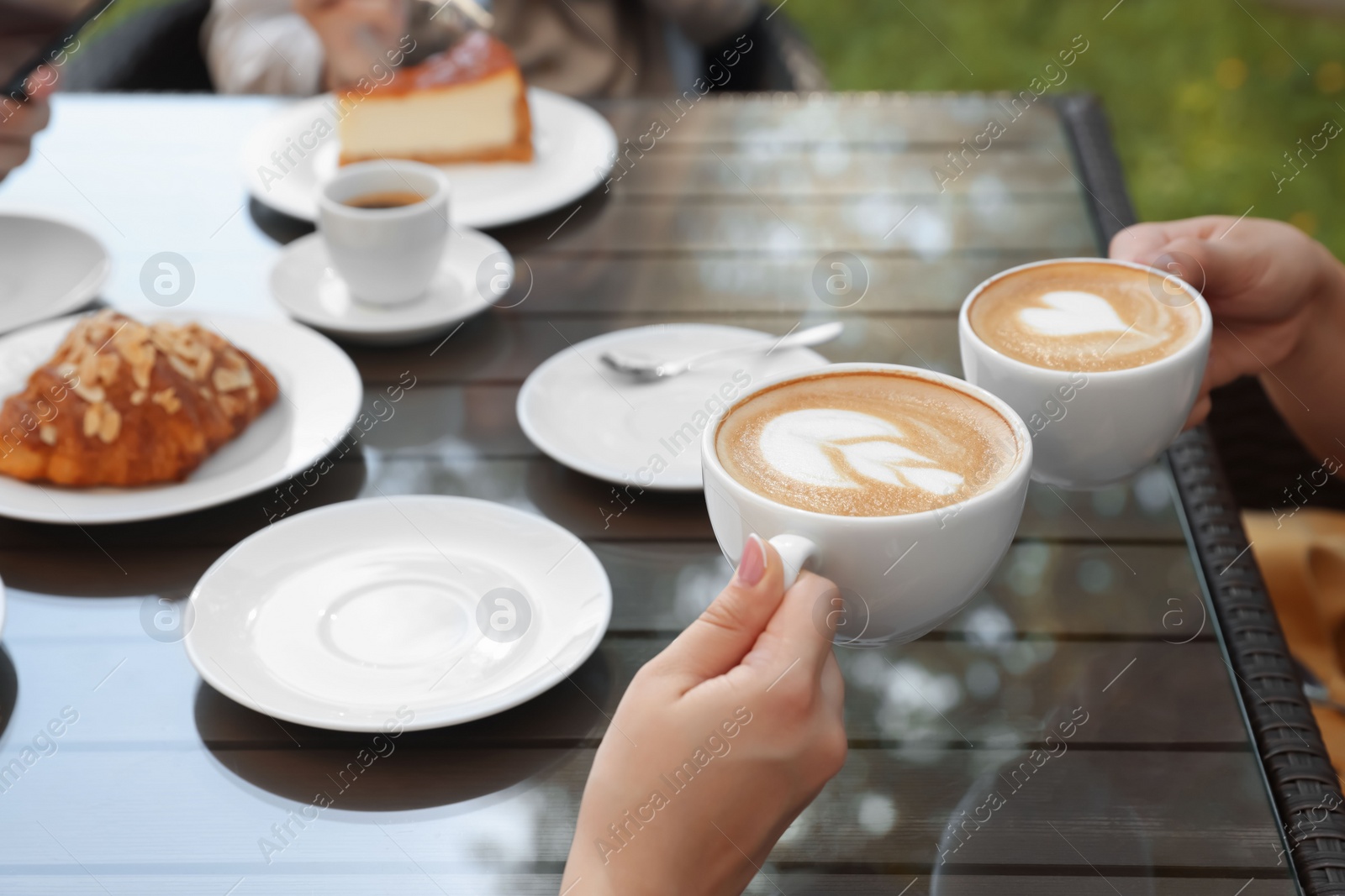 Photo of Friends drinking coffee at wooden table in outdoor cafe, closeup