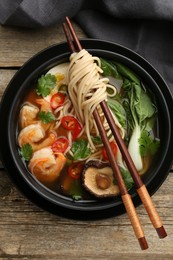 Photo of Delicious ramen with shrimps and chopsticks on wooden table, top view. Noodle soup