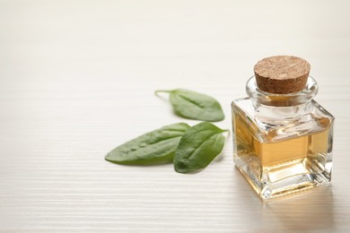 Photo of Essential oil of broadleaf plantain on light wooden table. Space for text