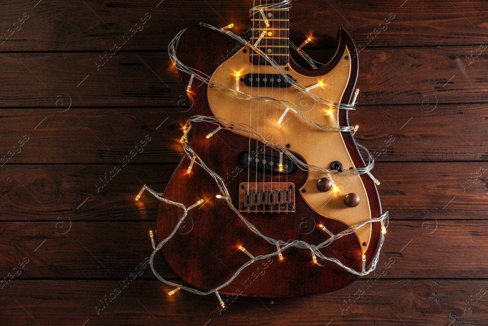 Photo of Guitar with fairy lights on wooden background. Christmas music concept
