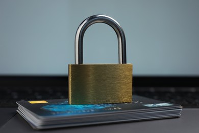 Photo of Cyber security. Metal padlock and credit cards on laptop, closeup