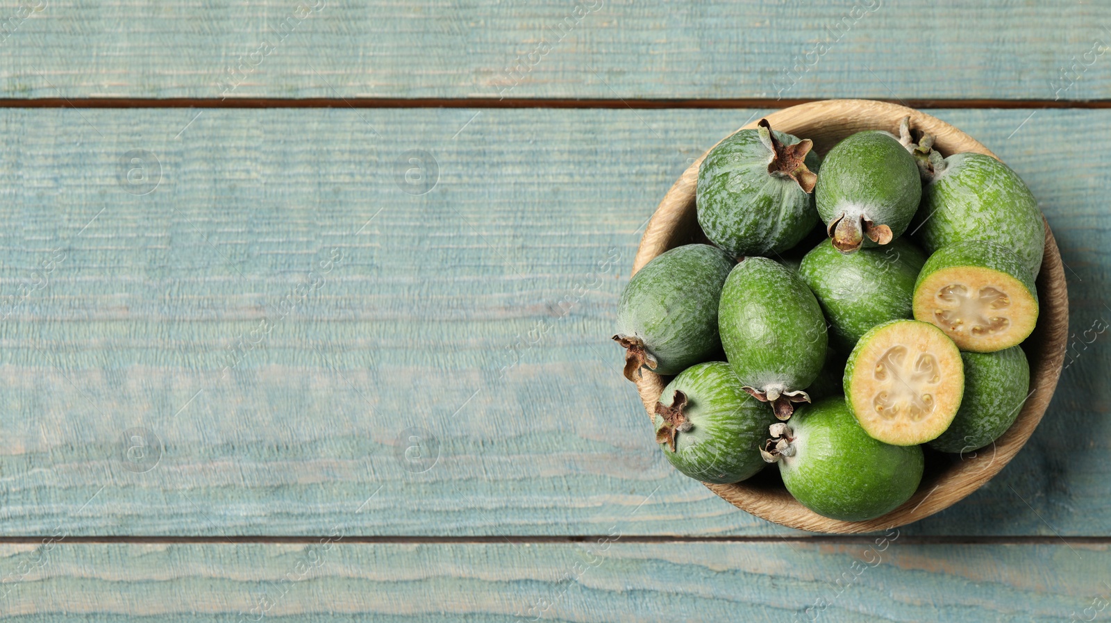 Image of Fresh green feijoa fruits in bowl on blue wooden table, top view with space for text. Banner design