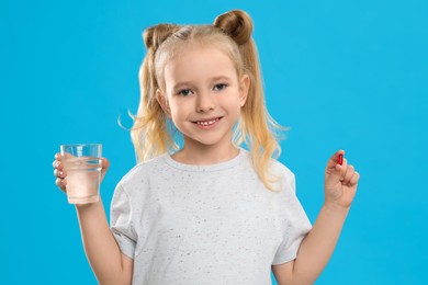 Photo of Little girl with vitamin pill and glass of water on blue background