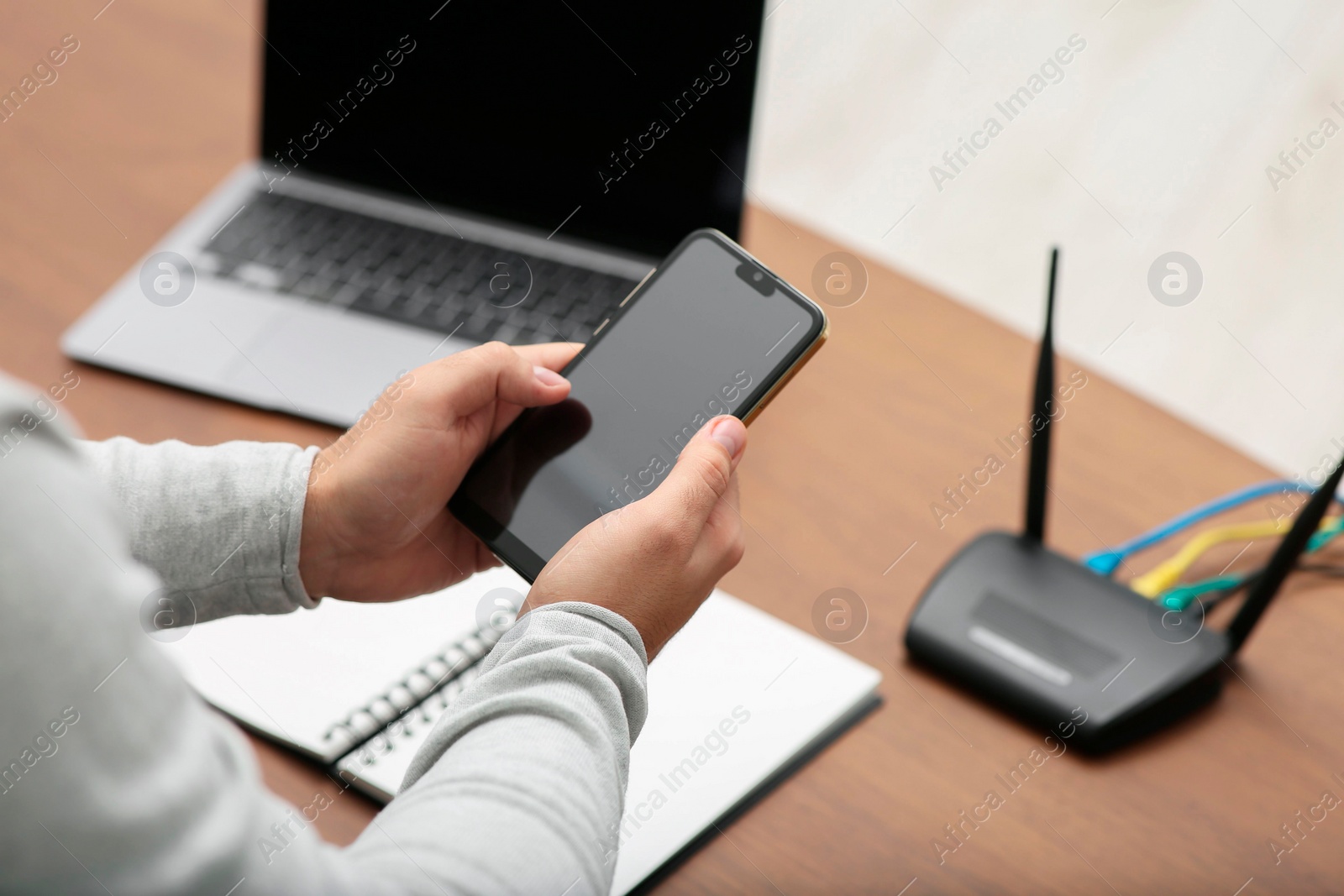 Photo of Man with smartphone and laptop connecting to internet via Wi-Fi router at wooden table, closeup