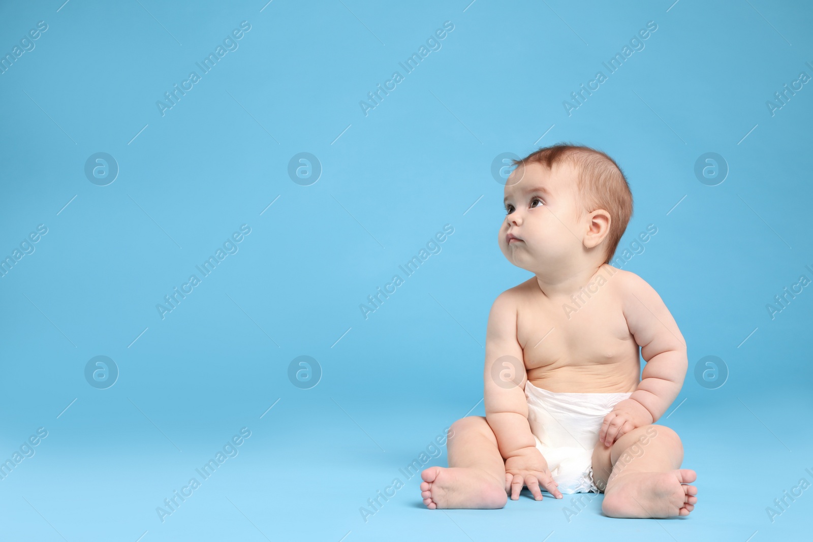 Photo of Cute little baby in diaper sitting on light blue background. Space for text