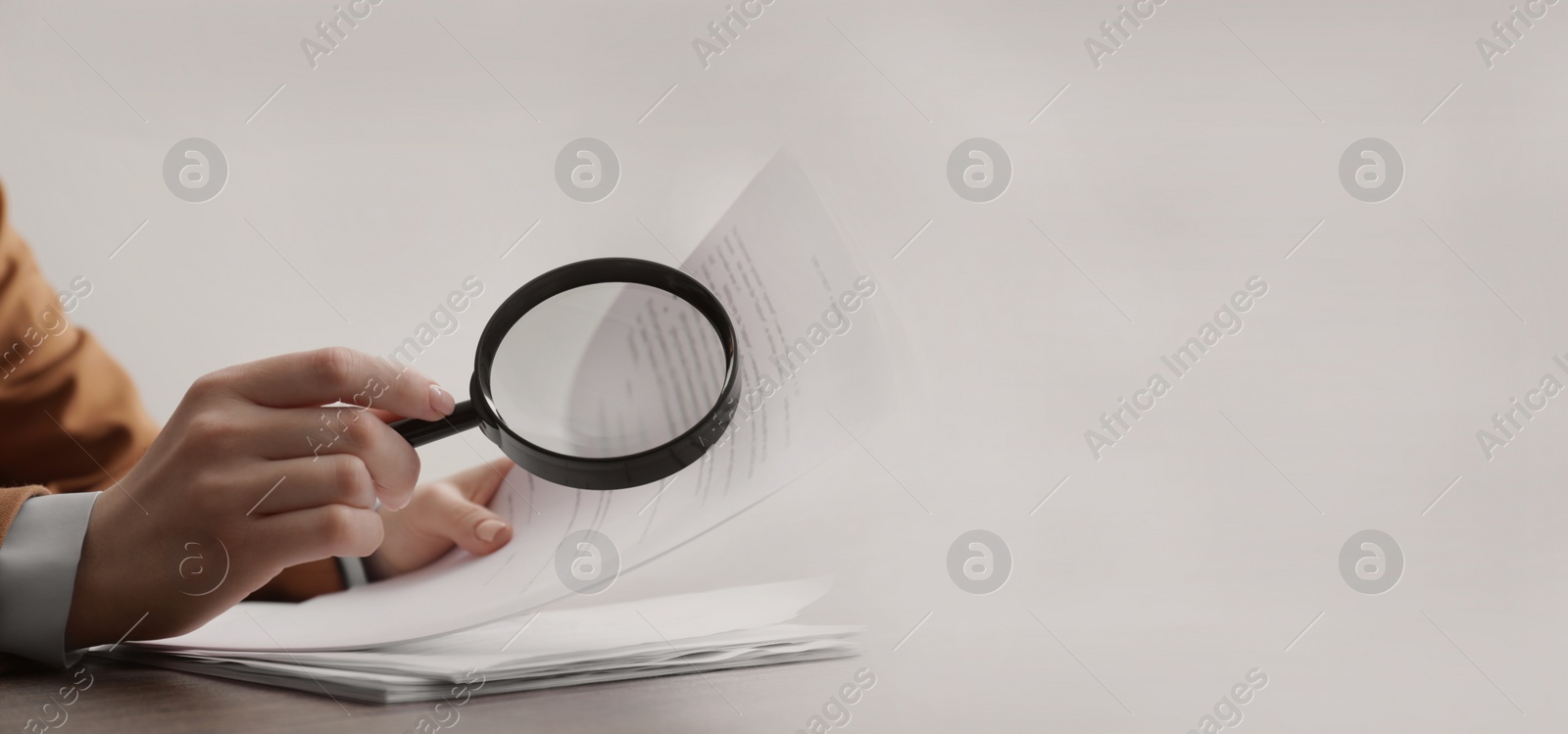 Image of Woman looking at documents through magnifier at wooden table, closeup. Banner design with space for text