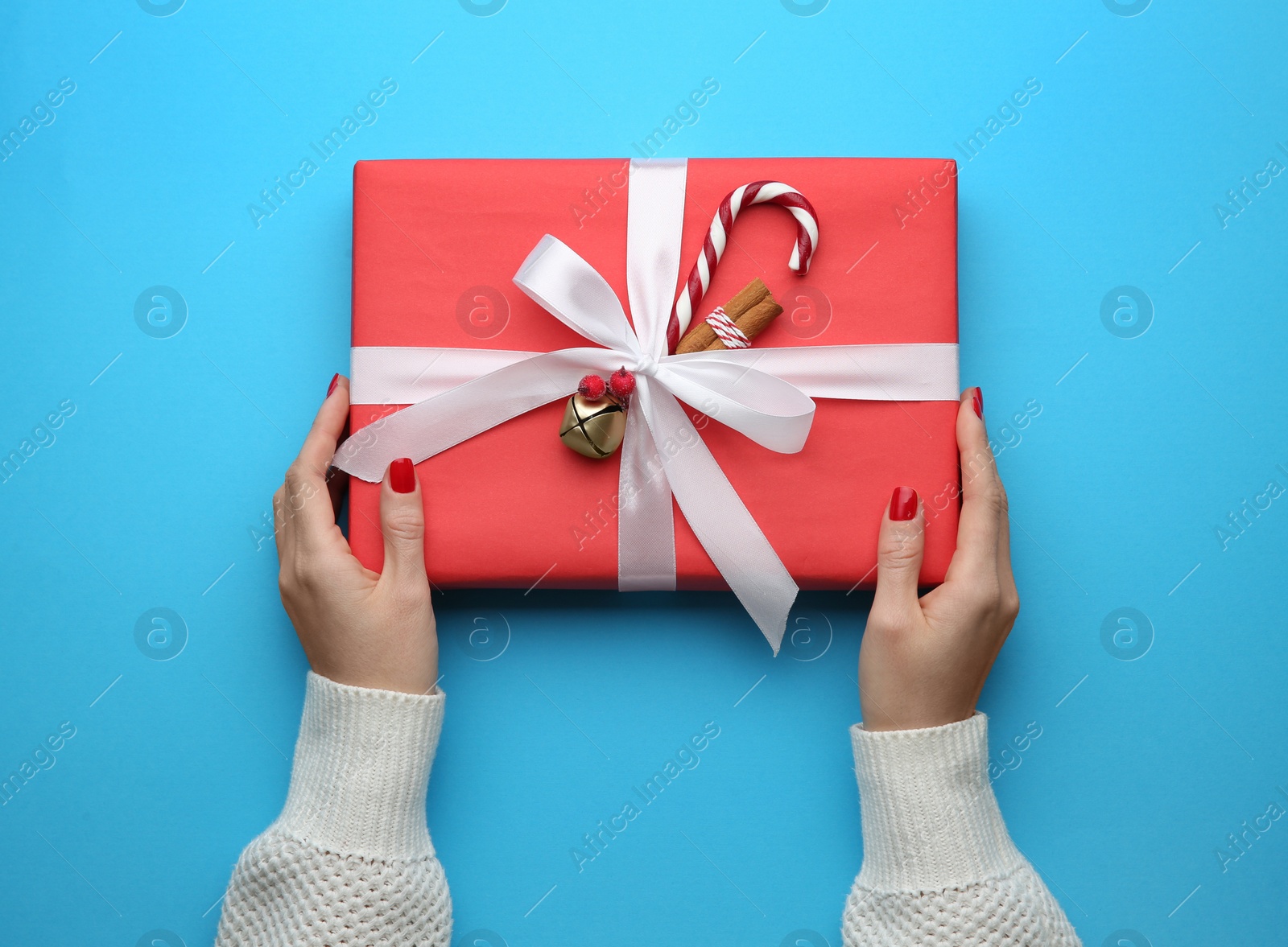 Photo of Woman holding Christmas gift box on light blue background, top view