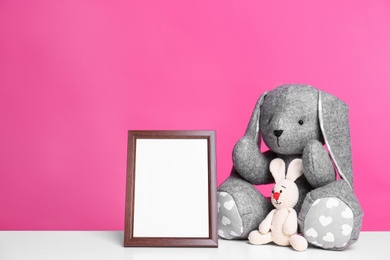 Photo of Photo frame and adorable toy bunnies on table against color background, space for text. Child room elements