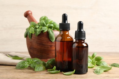 Photo of Bottles of basil essential oil near mortar with leaves and pestle on wooden table