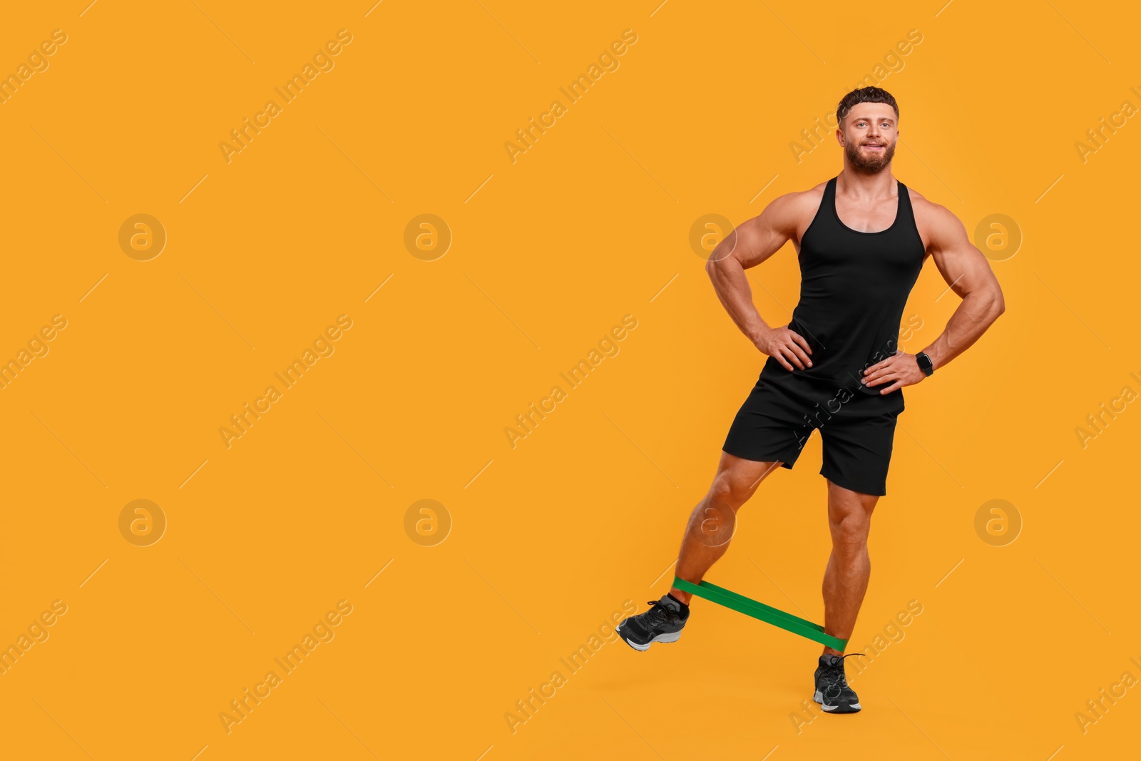 Photo of Young man exercising with elastic resistance band on orange background. Space for text