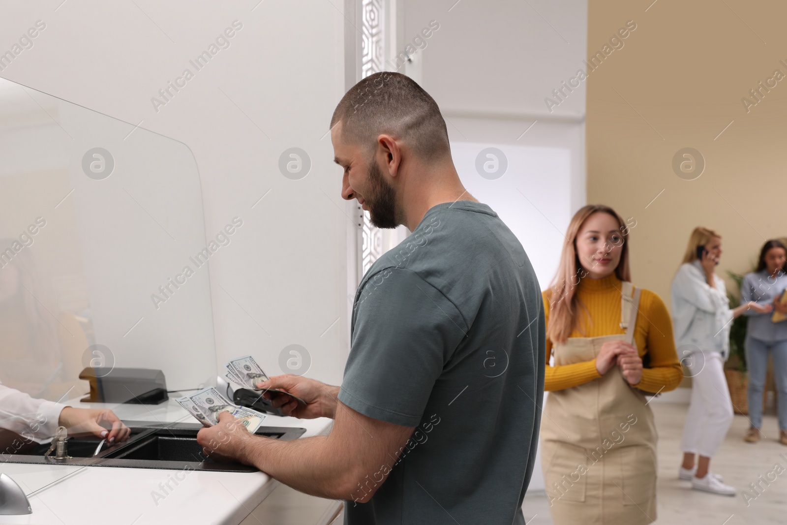 Photo of Man with money and other people in line at cash department window. Currency exchange