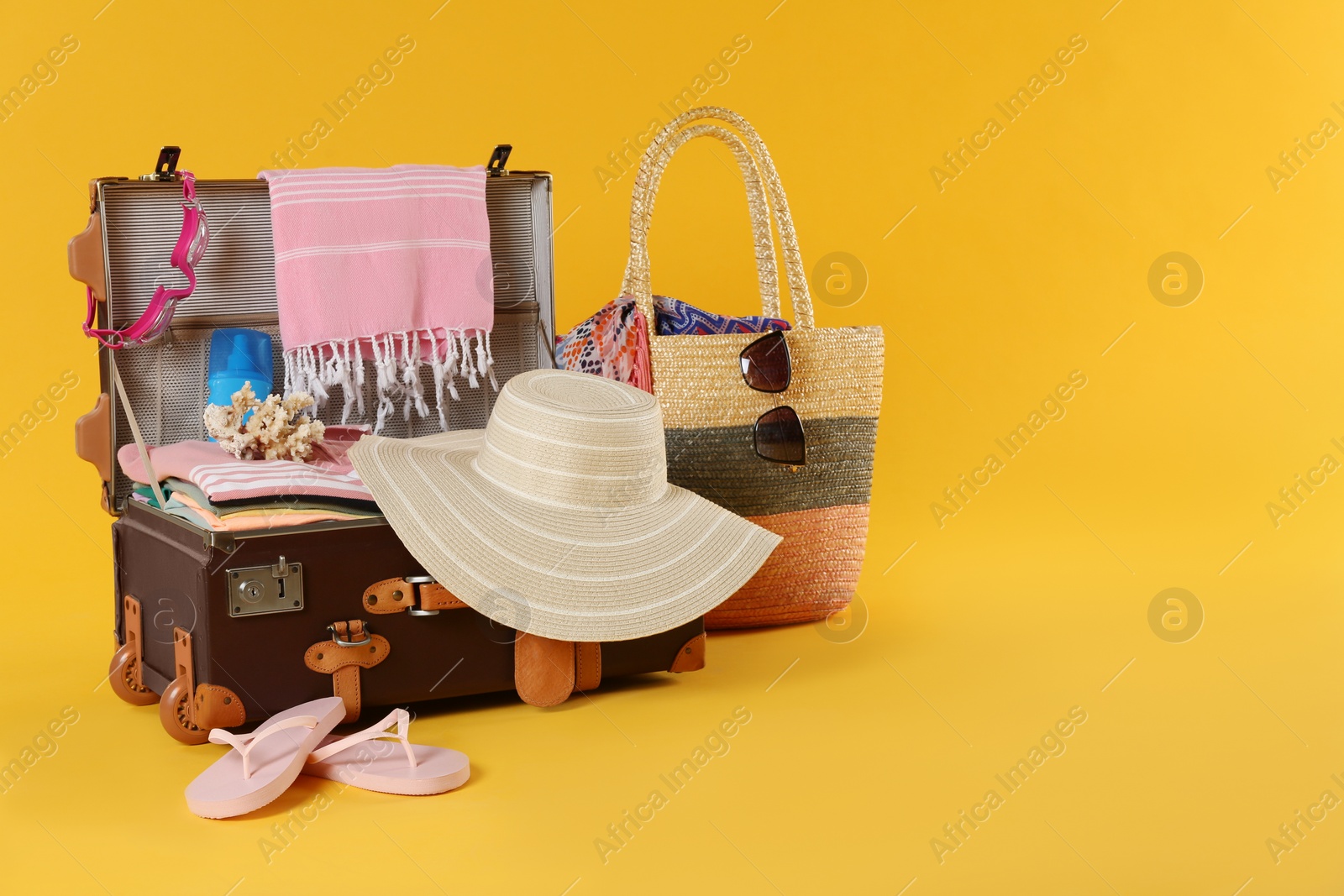 Photo of Bag and open vintage suitcase with different beach objects packed for summer vacation on orange background