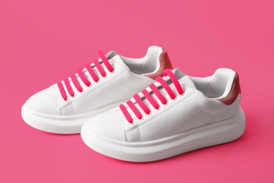Pair of stylish shoes with pink laces on color background