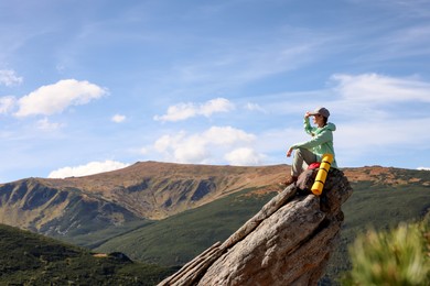 Photo of Young woman with backpack on rocky peak in mountains. Space for text