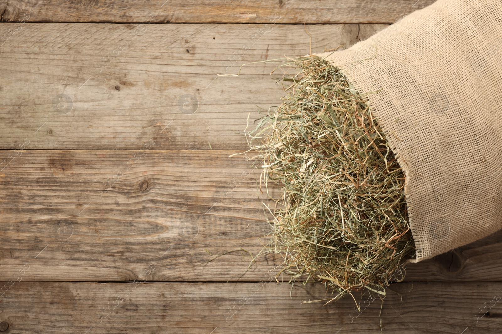 Photo of Burlap sack with dry herb on wooden table, top view. Space for text