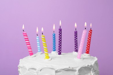 Delicious cake with cream and burning candles on purple background, closeup