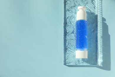 Bottle of cosmetic product on light blue background, top view. Space for text