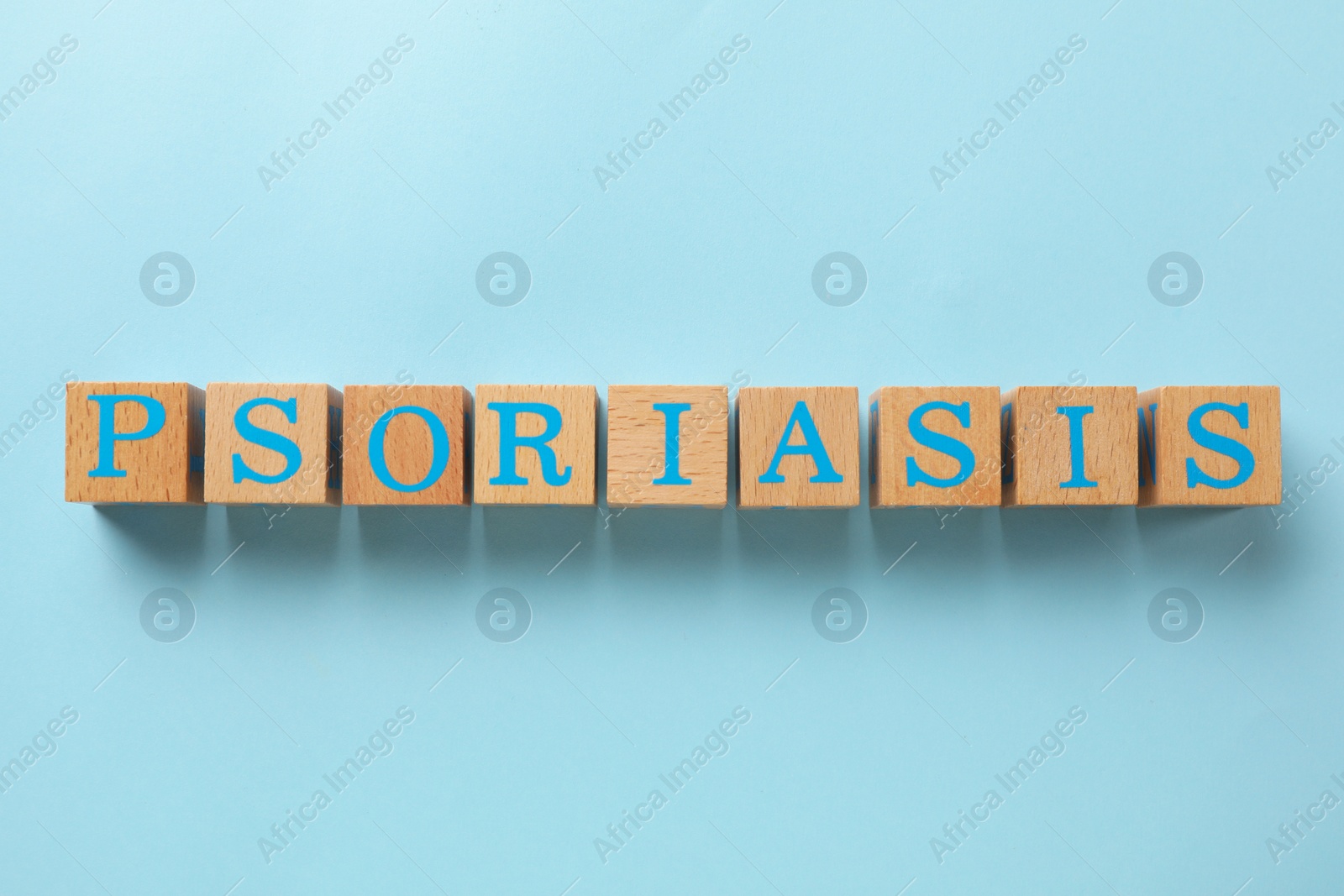 Photo of Word Psoriasis made of wooden cubes with letters on light blue background, top view