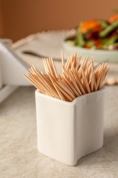 Holder with many toothpicks on beige table, closeup