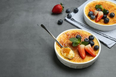 Delicious creme brulee with berries in bowl and spoon on grey table. Space for text
