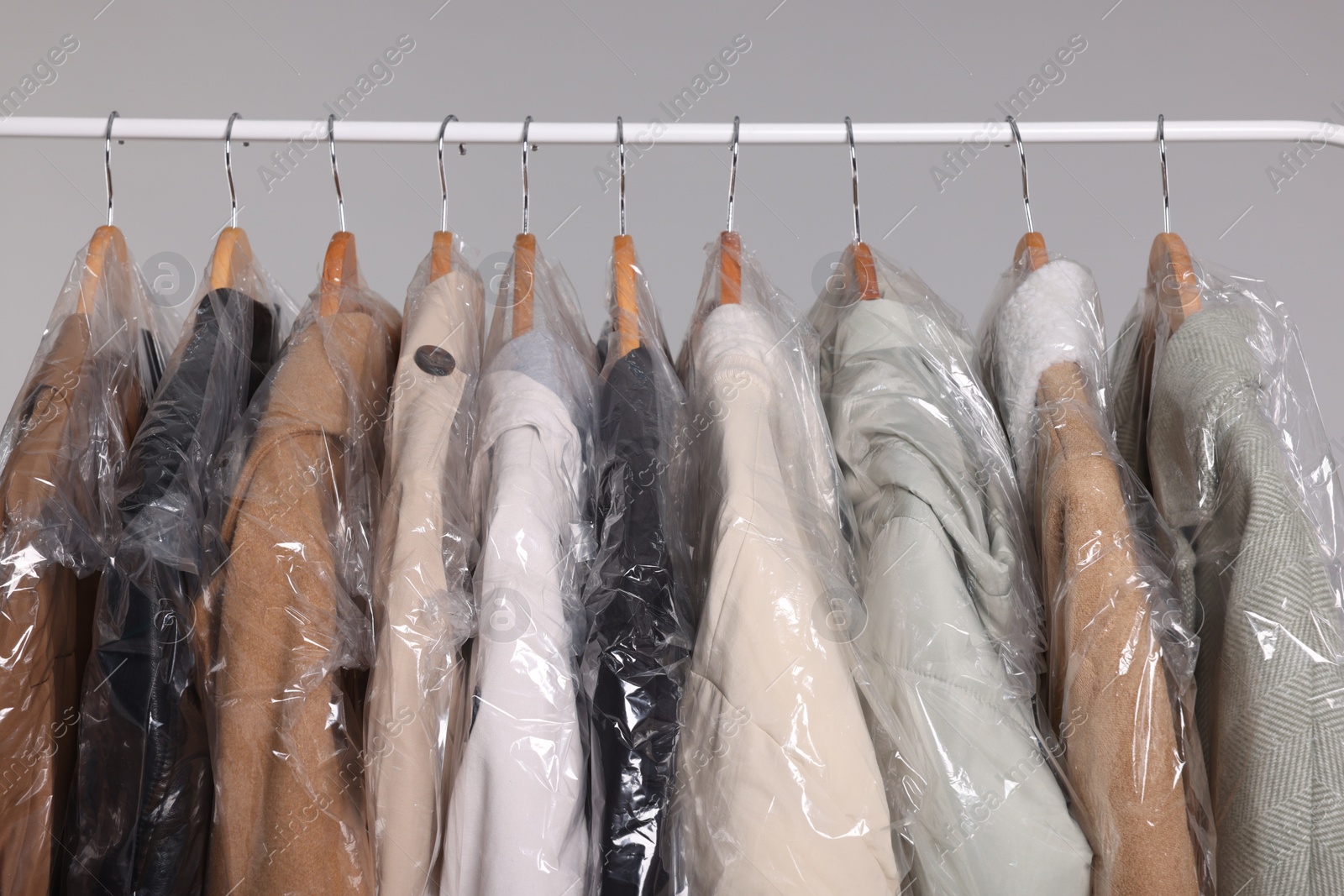 Photo of Dry-cleaning service. Many different clothes in plastic bags hanging on rack against grey background