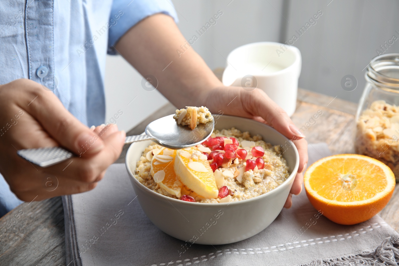 Photo of Woman eating quinoa porridge with nuts, orange and pomegranate seeds at table, closeup. Tasty breakfast