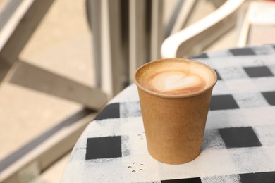 Photo of Takeaway paper cup with hot coffee on table outdoors, space for text