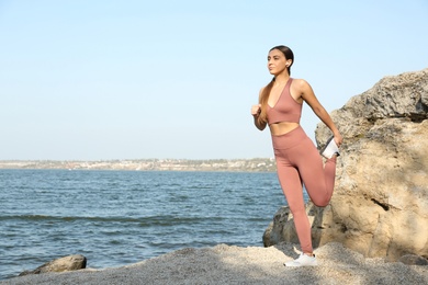 Photo of Young woman in stylish sports wear stretching on beach