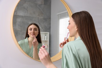 Beautiful young woman applying lipstick near mirror indoors