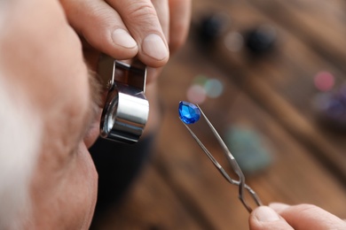 Photo of Male jeweler evaluating precious gemstone in workshop, closeup