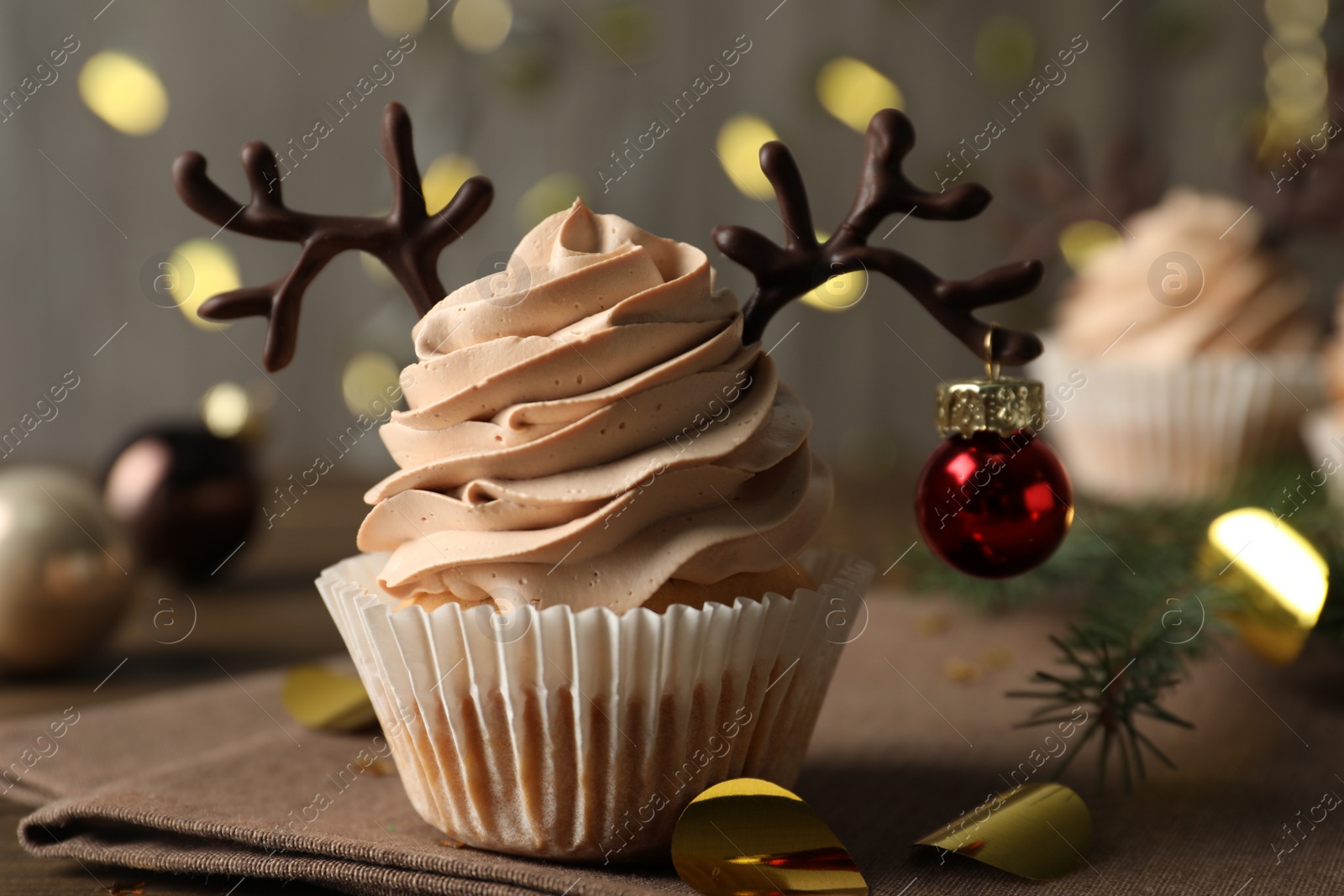 Photo of Tasty cupcake with chocolate reindeer antlers and Christmas bauble on table, closeup