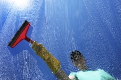 Photo of Woman cleaning glass with squeegee on sunny day