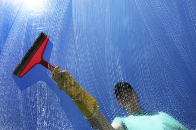 Woman cleaning glass with squeegee on sunny day