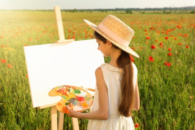 Photo of Little girl painting on easel in beautiful poppy field