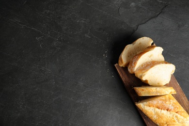 Photo of Board with bread on dark background, top view. Space for text