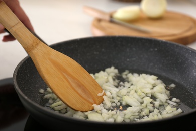 Photo of Woman frying chopped onion in pan, closeup