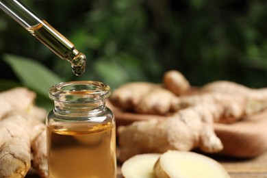 Photo of Dripping ginger essential oil from pipette into bottle on blurred background, closeup. Space for text