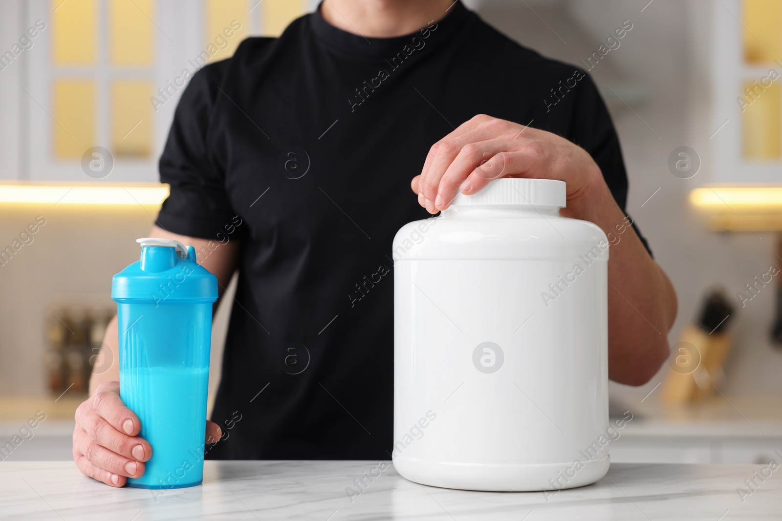 Photo of Young man with shaker of protein and powder at white marble table in kitchen, closeup