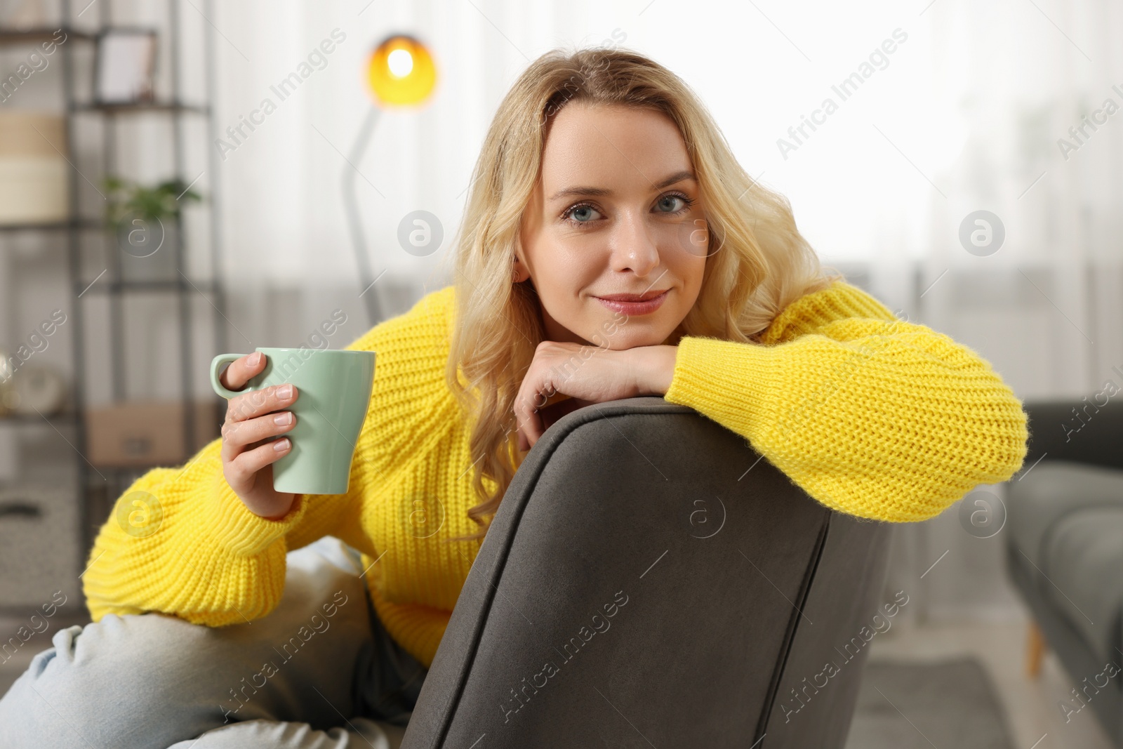 Photo of Beautiful woman in stylish warm sweater holding cup of drink at home