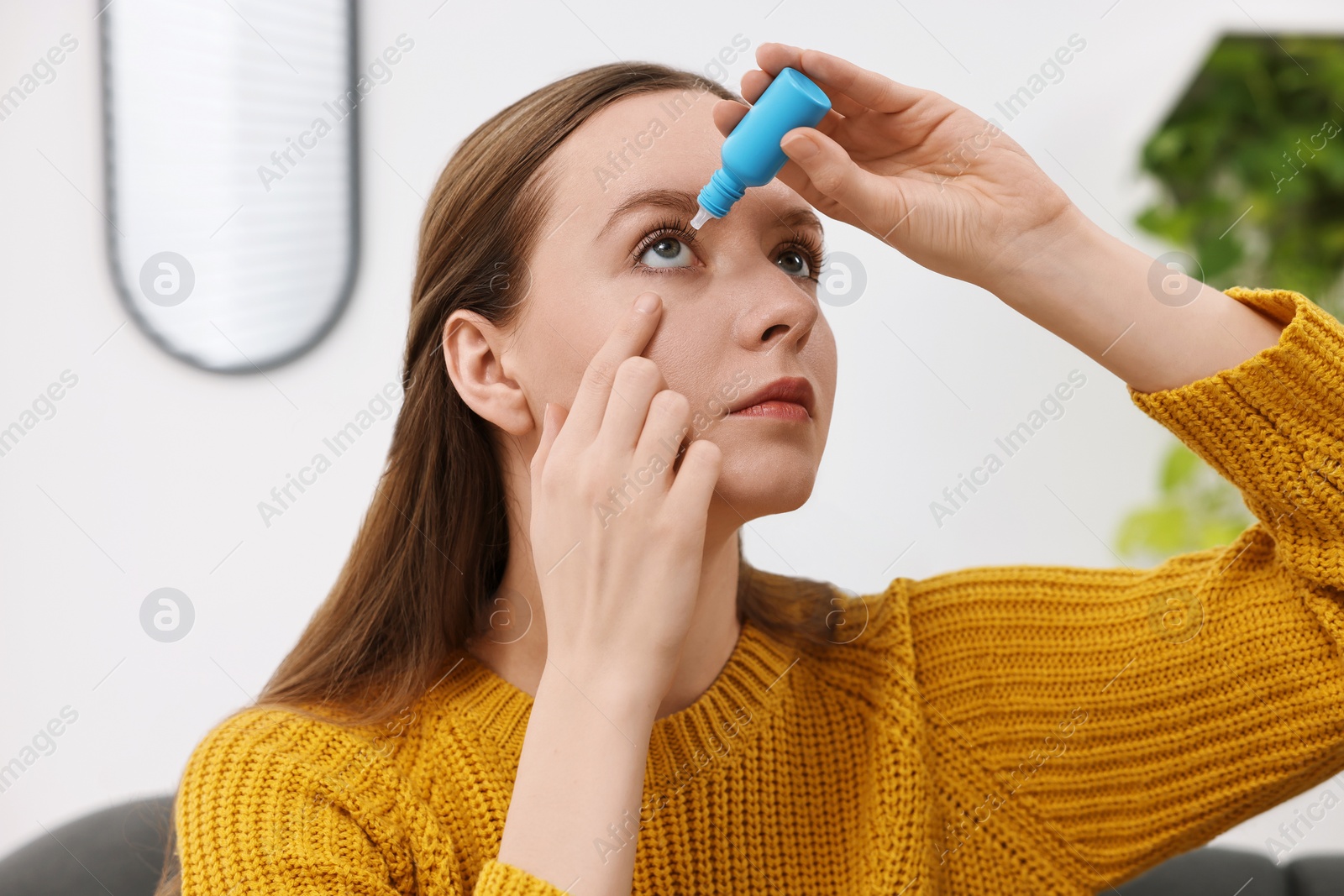 Photo of Young woman applying medical eye drops indoors