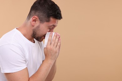 Photo of Allergy symptom. Man sneezing on light brown background. Space for text