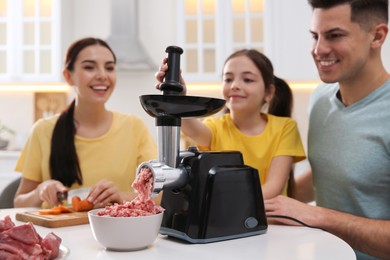 Photo of Happy family making dinner together in kitchen, father and daughter using modern meat grinder while mother cutting carrot